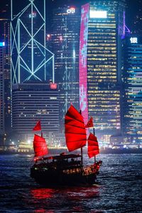 Red boat in river against illuminated buildings in city at night