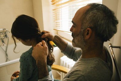 Father braiding daughter's hair in bathroom