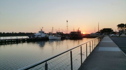 Boats moored at harbor against clear sky during sunset