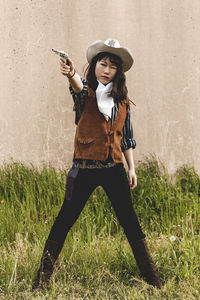 Young woman aiming gun while standing against wall
