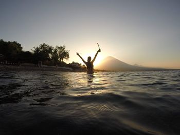 Silhouette person in sea against sky during sunset