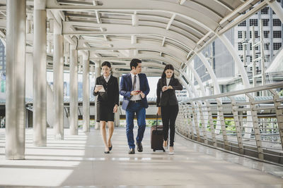 Full length of coworkers walking in office corridor