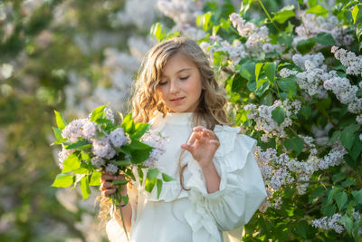 Young woman holding flower bouquet against plants