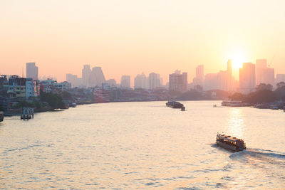 Sea by cityscape against sky during sunset