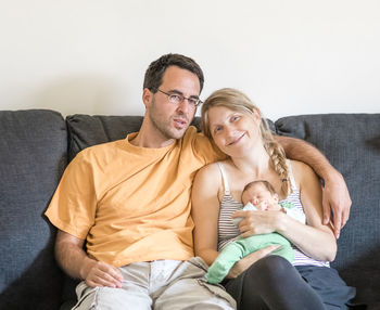 Smiling couple with baby sitting on sofa at home