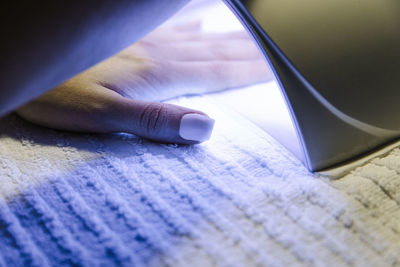 Unrecognizable female drying her acrylic nails under uv lamp on towel