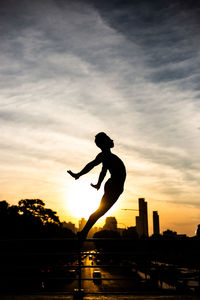 Silhouette man jumping over city against sky during sunset