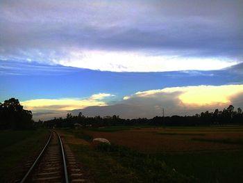 Railroad tracks on field against sky during sunset