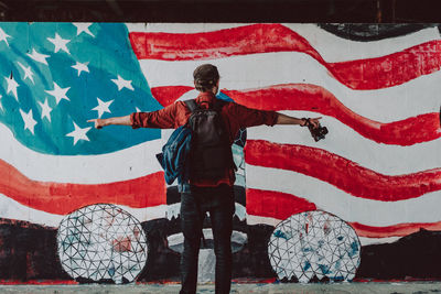 Rear view of man standing against painted american flag on wall