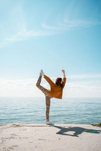 Full length of woman exercising on beach against sky