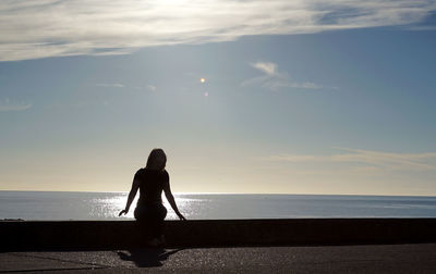 Woman sitting on retaining wall by sea against sky