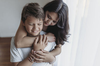 School-aged son being embraced by mother in natural light studio