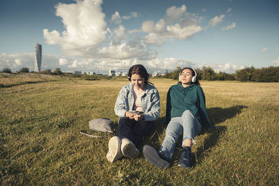 Female friends listening music through headphones while spending leisure time in park