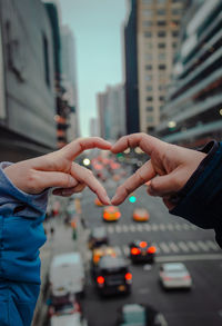 Close-up of hands making heart shape in city