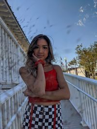 Portrait of young woman standing against railing