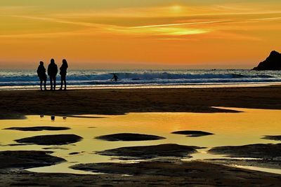 Silhouette people on beach against sky during sunset