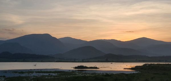 Scenic view of lake by mountains against sky during sunset