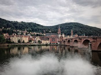 Arch bridge over river by buildings against sky