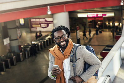 Smiling man using mobile phone while standing at airport