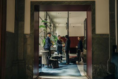 Young businesswoman greeting businessman while standing with colleagues in hotel lounge