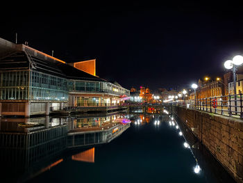 Illuminated bridge over river by buildings against sky at night