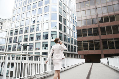 Female entrepreneur talking through mobile phone while walking on footbridge at downtown district