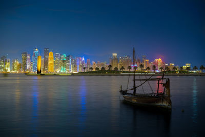 Illuminated city by river and buildings against sky