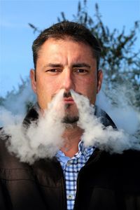 Portrait of man emitting smoke from nose against sky