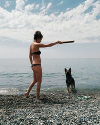 Woman with dog standing on beach against sky