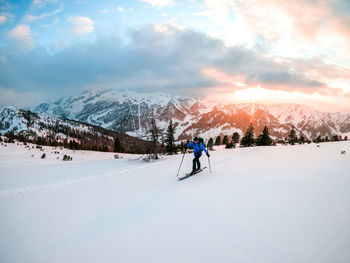 A man is having a sunset ski tour in zauchensee, austrian alps. sun is shining through the clouds.