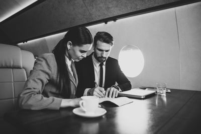 Colleagues discussing document while sitting at table in airplane