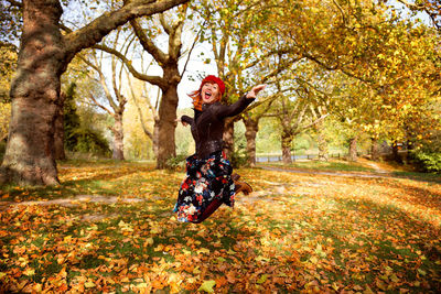 Cheerful woman jumping over field during autumn