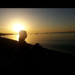 Silhouette woman sitting on beach against sky during sunset