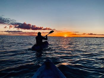 Silhouette woman kayaking in sea against sky during sunset