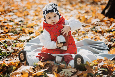 Happy little toddler baby daughter with red thermos and cup in autumn picnic in fall nature