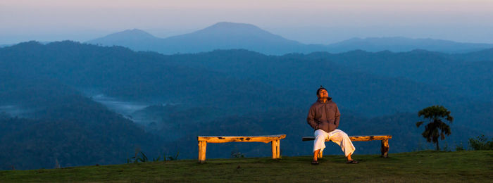 Man sitting on mountain against sky