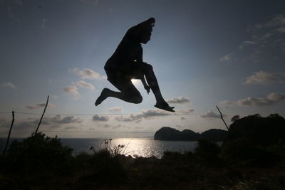 Silhouette man jumping on field against sky