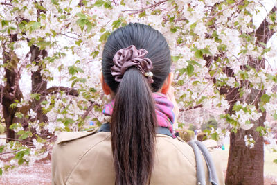 Rear view of woman standing against cherry blossom trees