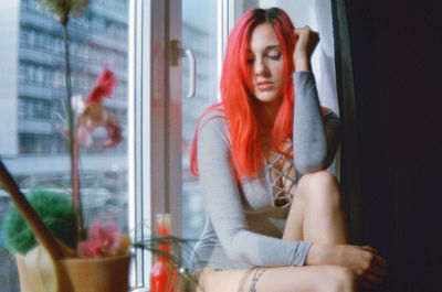 Thoughtful woman sitting on window sill at home