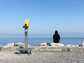 Woman sitting on lakeshore against clear sky