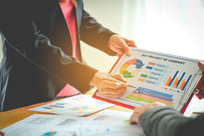 Midsection of businesswoman holding chart with colleague at office