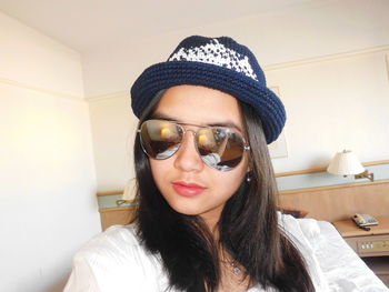 Portrait of young woman wearing sunglasses and hat at home