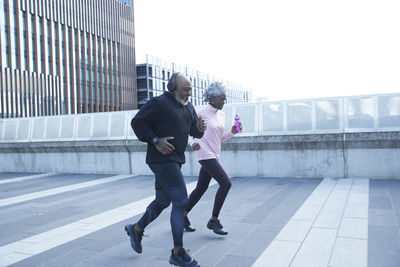 Man with headphones running by woman on footpath