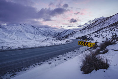 Road sign by snow covered mountain against sky