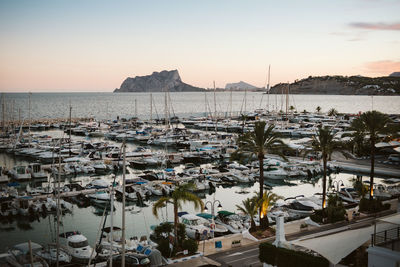 Sailboats moored at harbor against sky during sunset