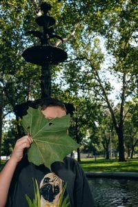 Portrait of boy covering his face with leaf near fountain in park