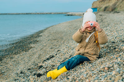 A little girl squinting photographs the autumn seascape on a childrens pink camera. the chil