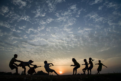 Silhouette people playing at beach against sky during sunset