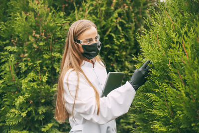 Young woman using phone while standing on plants