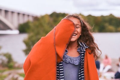 Cheerful girl with orange blanket enjoying in park during picnic